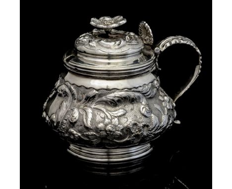 A George IV silver mustard pot of squat baluster form, with embossed foliate decoration and vacant central cartouche, S scrol