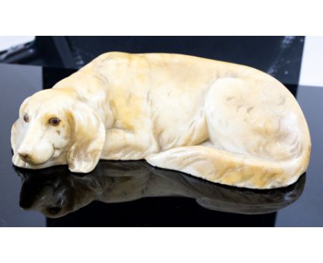 An alabaster paperweight model of a recumbent dog, early 20th Century, glass eyes, inset disc mark to base 'K&B', width 21cm