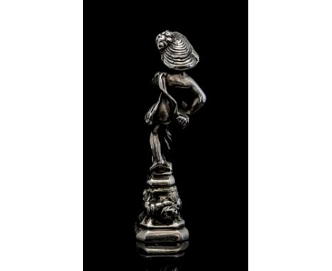 An early twentieth century silver pipe tamper or desk seal, modelled in the form of a boy holding a bunch of flowers seated a