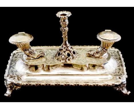 A Victorian silver desk stand, comprising two cast inkwells of cornucopia form, each with hinged cover and internal glass lin