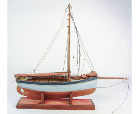 A scale model of a Falmouth work boat: standing rigged, the hull painted cyan above the waterline and red beneath, mounted on