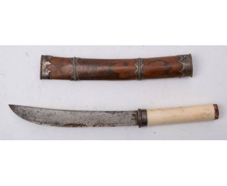 A Burmese dha dagger: the short curved back blade over a white metal hilt and one piece ivory grip, in a white metal bound wo