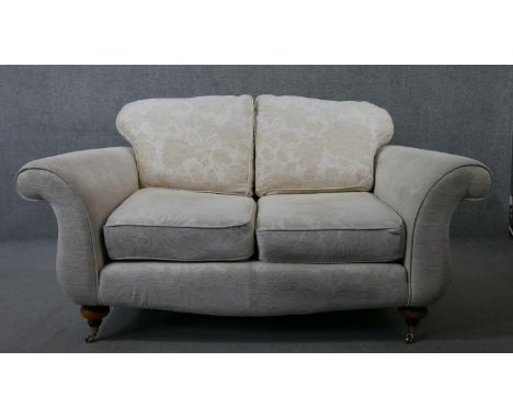A two seater Victorian style scroll arm sofa in floral upholstery on turned supports terminating in brass cup casters. H.91 W