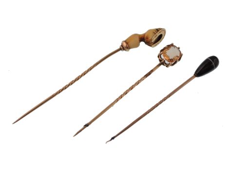 Three 19th century gold cravat stick pins. The pins having decorative finials to include a banded agate drop, a golden topaz,