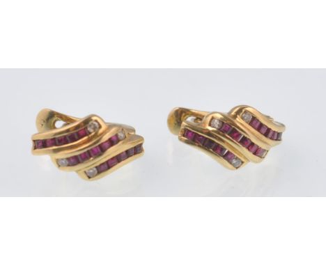 A pair of 18ct gold ruby and diamond channel set contemporary earrings. The cushion cut ruby stones flanked by diamonds. Tota