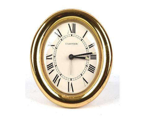 A Cartier gilt cased oval travel alarm clock the signed dial with black roman numeral hour markers and railway minute track c