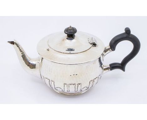 An Arts &amp; Crafts silver planished teapot, strapwork decorative panel to underside, ebony handle and finial, hallmarked by