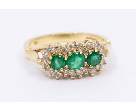 An emerald and diamond 18ct gold cluster ring, comprising three round cut claw set emeralds, within a border of round brillia