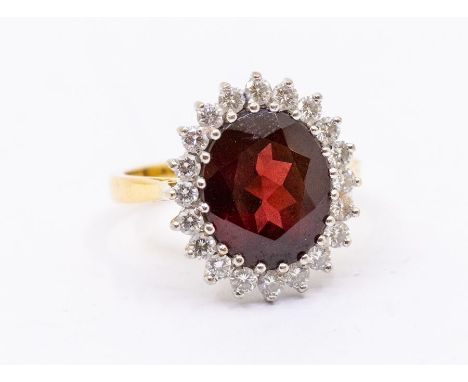 A garnet and diamond 18ct gold cluster ring, comprising a large oval cut garnet to the centre approx 9 x 11mm, within a diamo