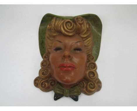 An Art Deco wall mask of female with blonde curly hair in a green hat, wearing red lipstick and a green and black bow at her 