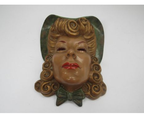 An Art Deco wall mask of female with blonde curly hair in a green hat, wearing red lipstick and a green bow at her neck, 31cm