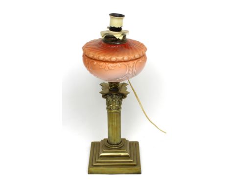 A brass oil lamp converted to electricity with Corinthian columns and stepped base beneath peach glazed ceramic reservoir, he