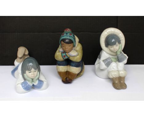 Two Lladró figures; one a seated girl in bobble hat, the other a seated girl in fur hood and a Nao figure of a girl lying wit