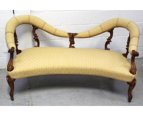 A Victorian walnut two-seater sofa with yellow upholstered back and seats, the frame carved with whorl and shell detail, on c