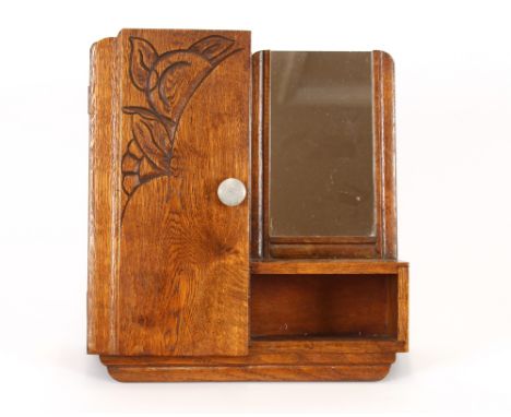 An oak Art Deco hanging wall cupboard with integral mirror and shelf, the door having carved foliate decoration, 39cm x 35cm 