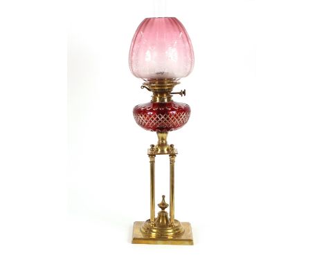 A late 19th Century brass oil lamp, raised on a four column base and square plinth, having ruby hobnail cut reservoir, the pi