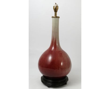 A Chinese sang de boeuf table lamp, with slender neck and bulbous body, with gilt metal mount to the top and carved wooden ba
