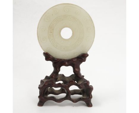 An Eastern mutton fat jade disc ring, decorated with stylized decoration to greek key centre, raised on a hardwood stand, dia