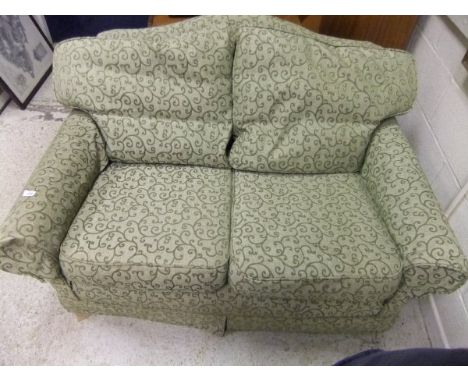 A modern two seat sofa with hump back and green self patterned scrolling upholstery