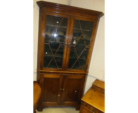 A 19th Century North Country oak and cross-banded corner cupboard, the moulded cornice above two glazed doors opening to reve
