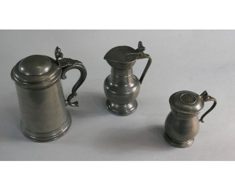Three 18th and 19th century pewter lidded flagons. One with acorn motifs to the handles and makers mark of a heart with HB an