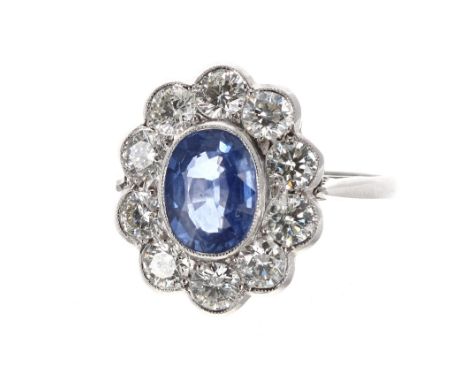 Impressive platinum sapphire and diamond oval cluster ring, the sapphire 1.35ct, in a surround of ten round brilliant-cut dia