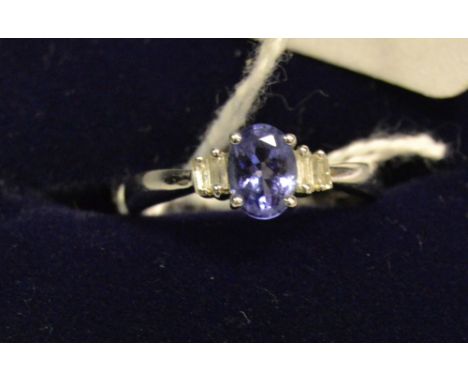 A tanzanite and diamond ring,  central oval tanzanite flanked by a pair of baguette and rhomboid cut diamonds to each shoulde