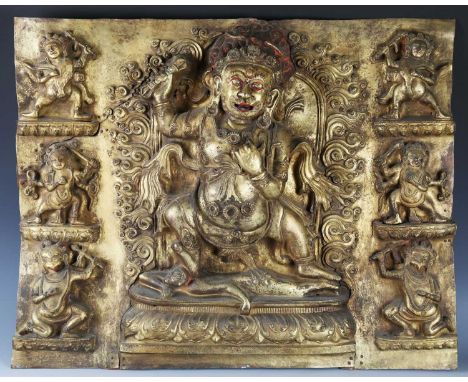 A Tibetan gilt bronze rectangular repoussé plaque, 15th century, depicting Vajrapani standing on a prostrate figure within a 