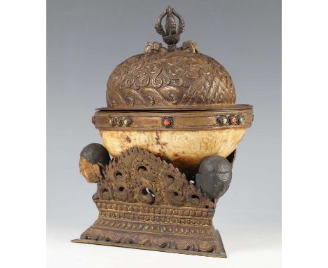 A Tibetan human skull kapala, probably 18th century, the brass domed cover repoussé decorated with lotus and scrolling tendri