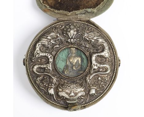 Tibet, a round travel altar, ghau; the silver alloy case with relief decor of dragons. With small brass Buddha figure and cot