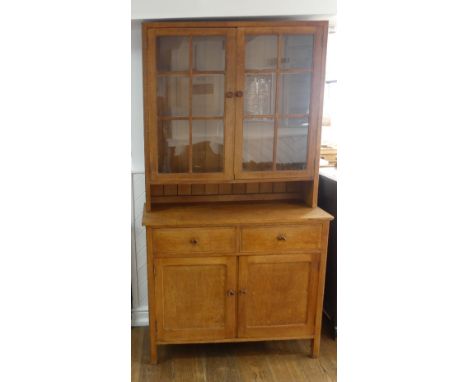 A Heals light oak Kitchen Dresser, the upper section with three tier plate rack enclosed by glazed doors, the base with two f