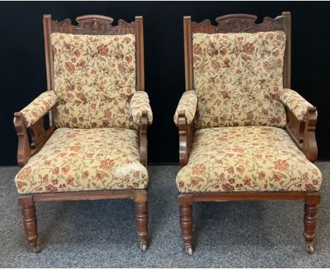 A pair of Edwardian carved oak library chairs, carved cresting rail and arms, button back and stuffed over seats, with floral
