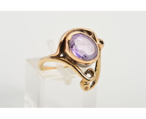 A 9CT GOLD AMETHYST DRESS RING, designed as an oval collet set amethyst set on a diagonal angle within an open scrolling surr