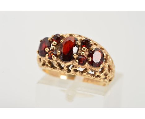 A 1970'S 9CT GOLD GARNET RING, designed as three graduated oval garnets within claw settings interspaced by a total of four c