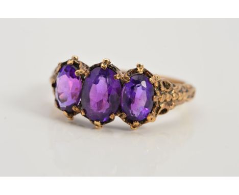 A 9CT GOLD AMETHYST THREE STONE RING, designed as three graduated oval amethysts within claw settings with scrolling detail t