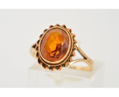 A 9CT GOLD CITRINE RING, designed as an oval citrine within a millegrain setting and double rope twist surround to the bifurc