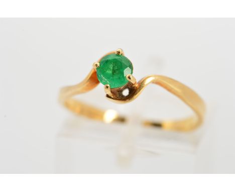 AN EMERALD RING, designed as a circular emerald within a four claw setting to the cross over surround, stamped 18k, ring size