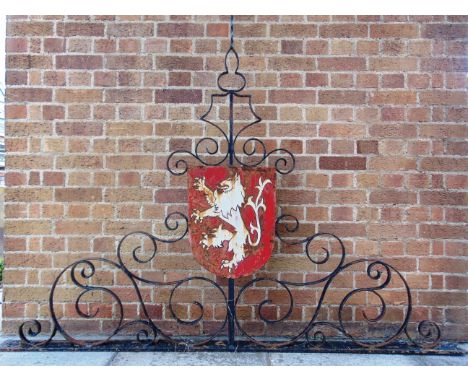 A WROUGHT IRON GATE OR WALL SURMOUNT  incorporating a painted shield, overall 145cm high, 196cm wide.