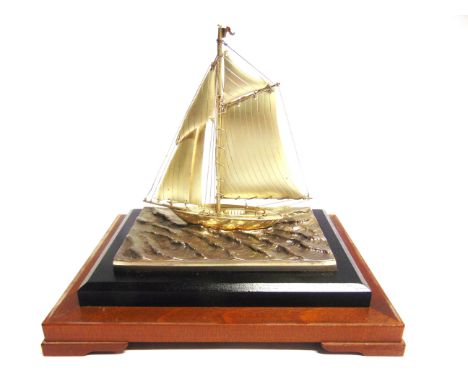 A SILVER PLATED MODEL OF A YACHT  set to a wave-top plinth base, overall 13cm long, in a glazed case, 21cm high, 20cm wide, 1