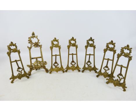 A set of six cast brass, easel plate stands and one larger example, largest approximately 27 cm (h). [W]