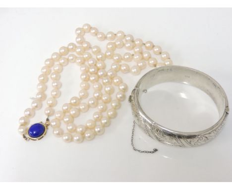 A single row uniform cultured pearl necklace, with a gold and lapis lazuli cabochon clasp, marked 14k, and a silver bangle wi