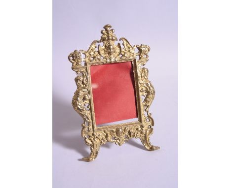 A CAST GILT METAL EASEL PICTURE FRAME, having pierced and moulded figural side supports with mask head top and bottom on scro