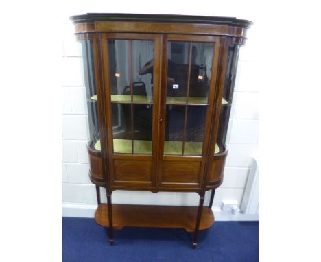 AN EDWARDIAN MAHOGANY INLAID TWO DOOR DISPLAY CABINET, with bowed end sections and lower shelf on square tapering supports wi