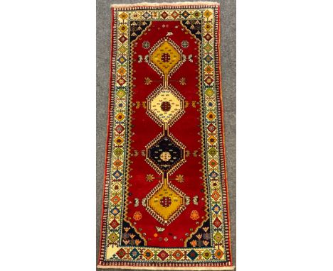 A South-west Persian Qashgai runner carpet, hand-knotted with a row of four hexagon-shaped medallions, within a deep red fiel