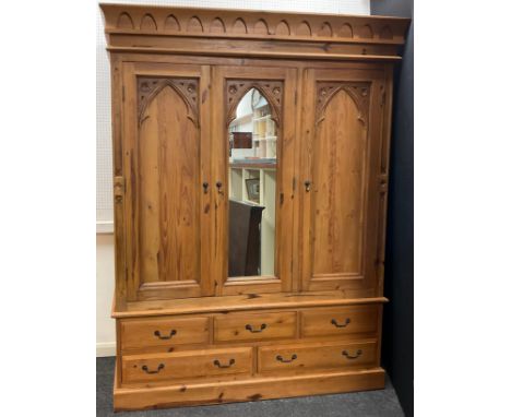 A Gothic style pine triple wardrobe, central dressing mirror door, flanked by a pair of doors with Gothic arch carved panels,