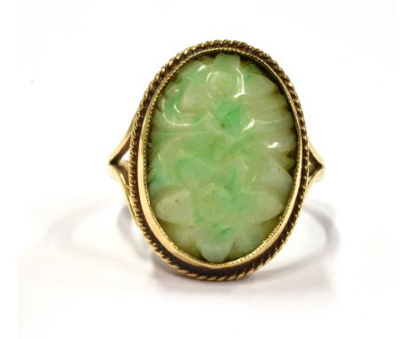 A 9CT GOLD JADE (?) STONE COCKTAIL RING With the oval floral carved stone measuring 2cm by 1.5 cm including gold mount, the s