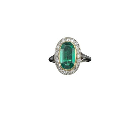 An oval-shaped emerald and diamond cluster ring, the oval-shaped emerald set within a surround of circular-cut diamonds in ca