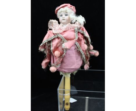 AN EARLY 20TH CENTURY COMBINATION DOLL WITH WHISTLE HANDLE, having a bisque head and pink fabric jester style costume, 34cm h