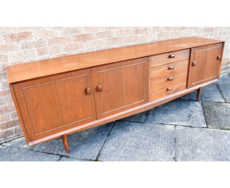 A 1960S TEAK SIDEBOARD  fitted with four drawers flanked to one side with drop-down cupboard enclosing sliding shelf, the oth