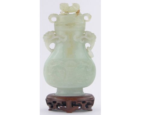 A Chinese pale green jade vase and cover,relief carved allover with dragons and scrolls, hardwood stand, height overall 20cm,
